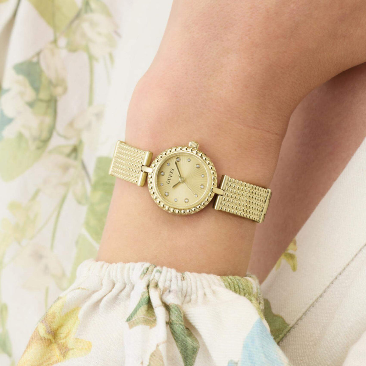 Γυναικείο ρολόι Guess Holly GW1017L2 φορεμένο με χρυσό μπρασελέ ανάγλυφης υφής και χρυσό καντράν με ζιργκόν.